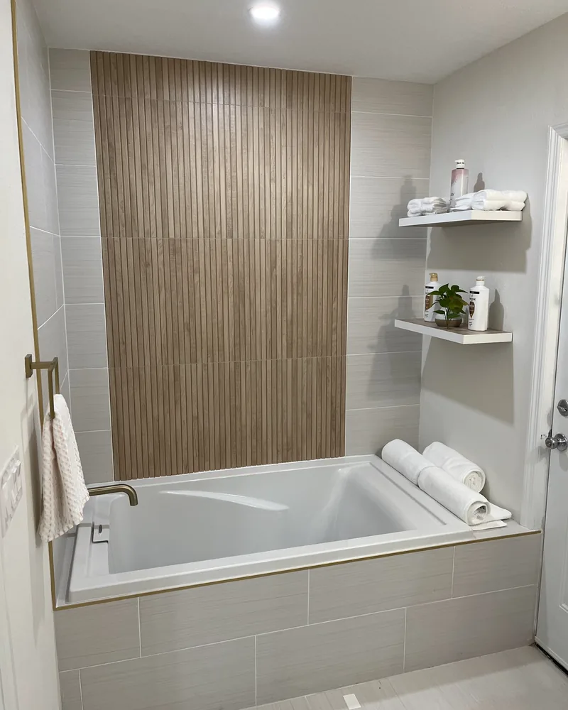 Finished bathroom by ProCare Contracting: a soaking tub beneath a fluted wood-tile feature wall, with brass fixtures and floating shelves