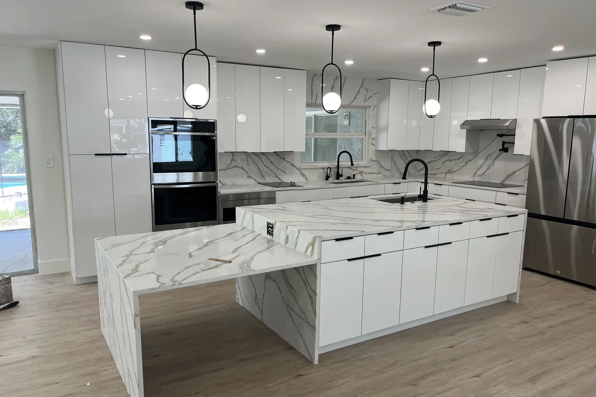 Renovated kitchen with a marble waterfall island and white cabinetry by ProCare Contracting