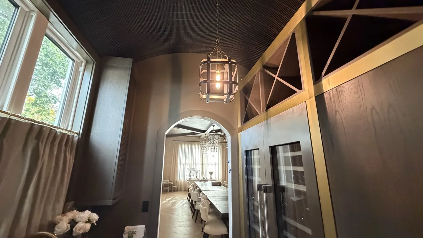 Custom butler's pantry with a brass wine rack, barrel-slat ceiling and an arched view to the dining room