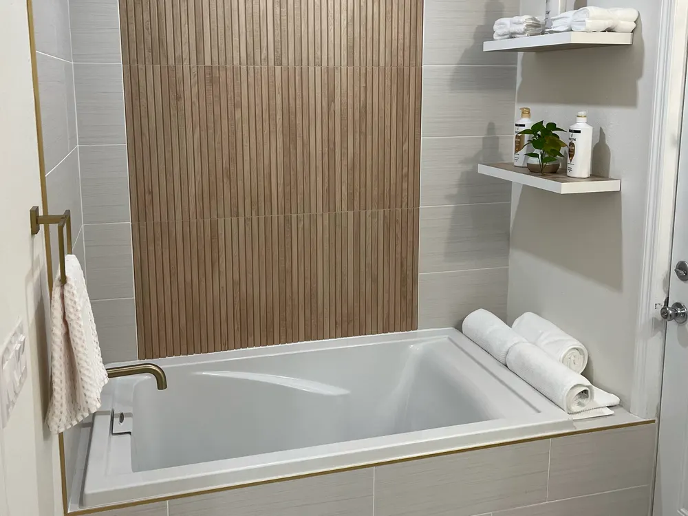Soaking tub beneath a wood-slat feature wall with brushed-gold fixtures and floating shelves