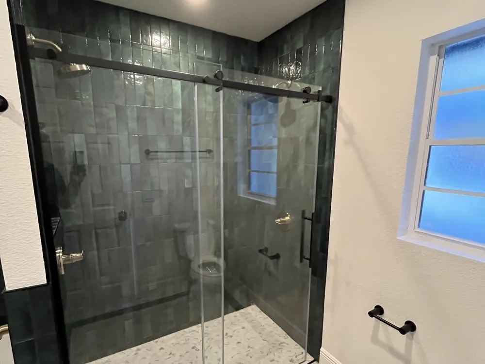 Walk-in shower with green zellige tile and frameless sliding glass